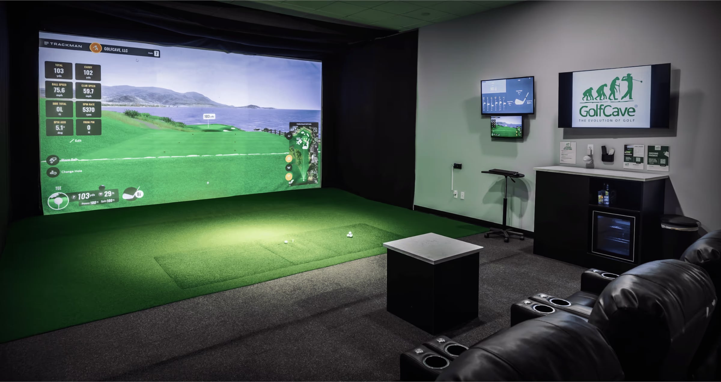GolfCave Clark — A private Cave room end to end: lit screen, hitting turf, black leather sofa against the s