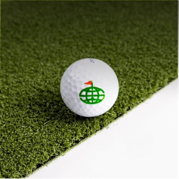 A golf ball resting on the edge of ST57 putting turf against a white background